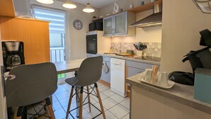 A compact kitchen with a coffee maker, microwave, oven, and a dishwasher. There are two bar stools and a small dining table. - Cozy Retreat for 4 with South-Facing Balcony, Garage, and Easy Access to Nature and Local Attractions (Gérardmer)