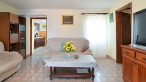 A living room with a sofa, a coffee table with a vase of flowers, a television, and wooden cabinets. - House 2063/32559 (Istria - Poreč), 6000m from the beach (Poreč)