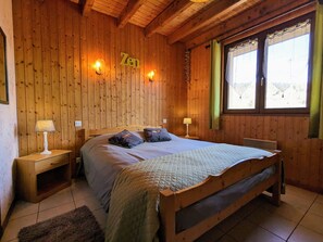A wooden-paneled bedroom with a bed, two bedside lamps, a window with curtains, and a wall-mounted sign.