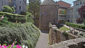 A historic stone tower with a pointed roof, surrounded by lush greenery and a cobblestone path. - Cozy Cottage Near Epinal: Nature, City, and Equestrian Center Nearby (Chantraine)
