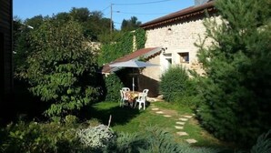 A stone building with a tiled roof, surrounded by lush greenery and a stone pathway leading to a seating area with chairs. - Cozy Cottage Near Epinal: Nature, City, and Equestrian Center Nearby (Chantraine)