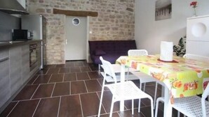 A compact kitchen with a stone wall, a dining area with a table and chairs, and a built-in oven. - Cozy Cottage Near Epinal: Nature, City, and Equestrian Center Nearby (Chantraine)