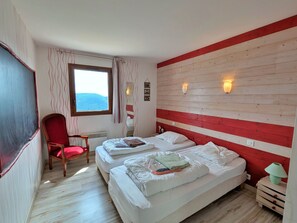 Une chambre d’hôtel avec deux lits, un fauteuil rouge, une fenêtre donnant sur un beau paysage et un lambris en bois sur le mur.
