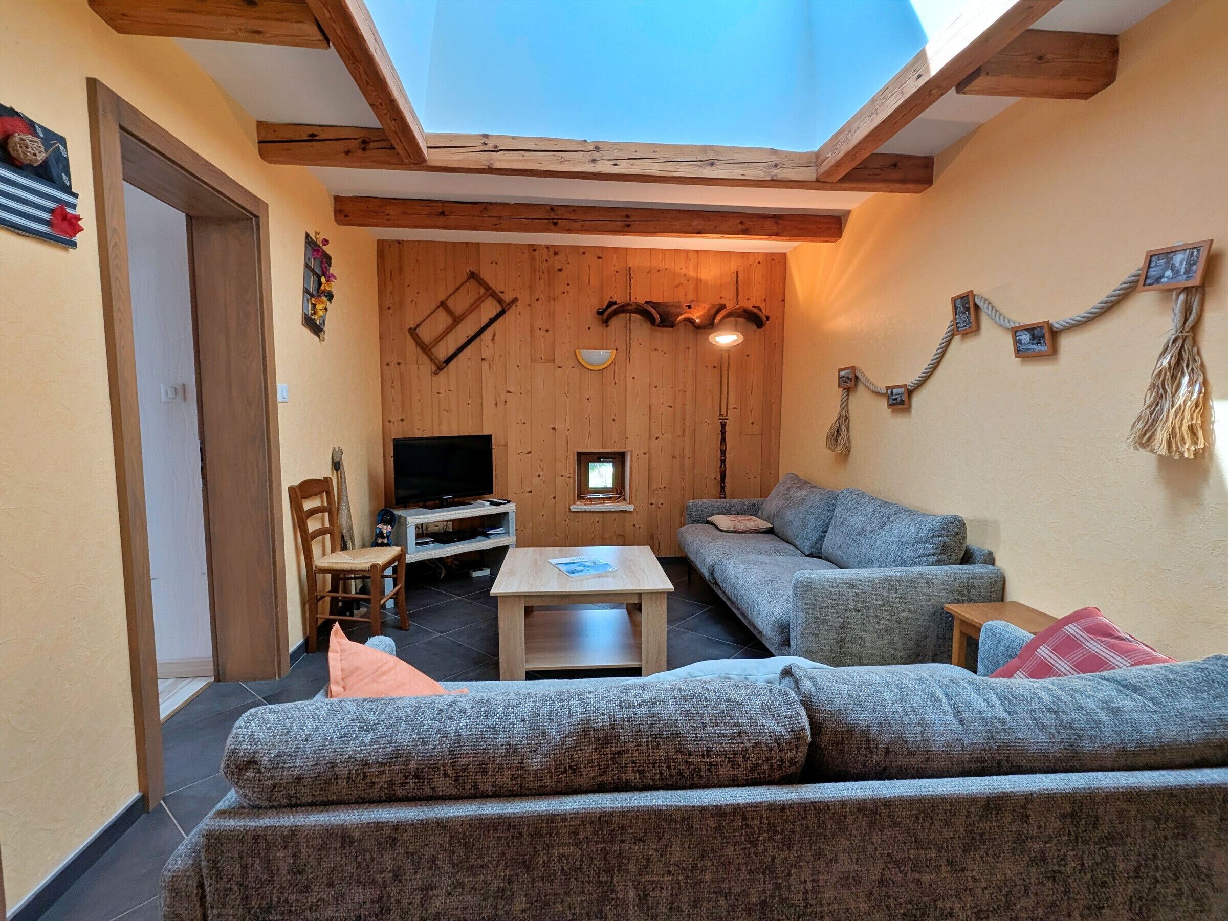 Ein gemütliches Wohnzimmer mit Holzbalkendecke, einem Fernseher, einer Couch und einem kleinen Tisch.