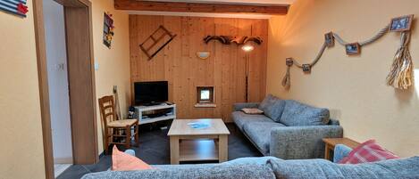 Ein gemütliches Wohnzimmer mit Holzbalkendecke, einem Fernseher, einer Couch und einem kleinen Tisch.