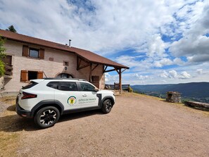 Un SUV blanco estacionado frente a un edificio rústico con un muro de piedra y techo de tejas.