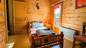 A wooden cabin room with a bed, a chair, a small table, and a window with a view. - Cozy Chalet Near Ski Slopes and Lake, Sleeps 7, WiFi, Fireplace, Large Garden, Garage (Le Menil)