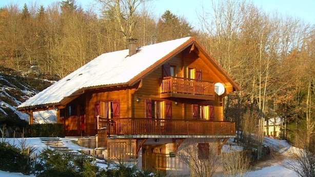 A wooden cabin with a balcony, surrounded by snow and trees. - Cozy Chalet Near Ski Slopes and Lake, Sleeps 7, WiFi, Fireplace, Large Garden, Garage (Le Menil)