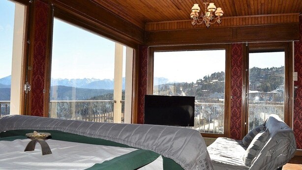 Una habitación con una cama, televisión y amplias ventanas que ofrecen vistas a la montaña.