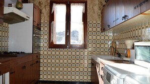 Una cocina con paredes de baldosas estampadas, armarios de madera, una ventana y electrodomésticos básicos.