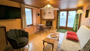 A cozy living room with a fireplace, wooden floors, a green armchair, a sofa, and a television.