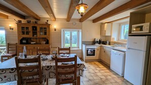 Eine Küche mit Holzbalken, einem Esstisch mit Stühlen, einem Herd, einer Mikrowelle und einem Kühlschrank.