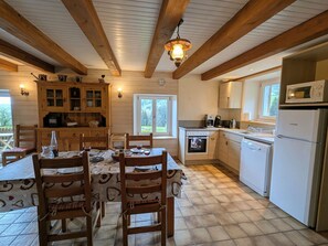 Eine Küche mit Holzbalken, einem Esstisch mit Stühlen, einem Herd, einer Mikrowelle und einem Kühlschrank.