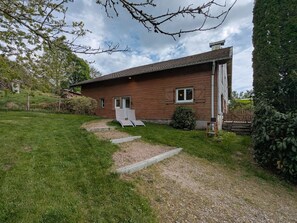 Une maison de plain-pied en briques, avec une porte d’entrée, une petite fenêtre et une allée pavée menant à une chaise blanche.
