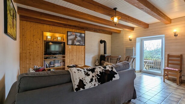 Ein gemütliches Wohnzimmer mit Sofa, Fernseher, Kamin und Blick ins Freie.