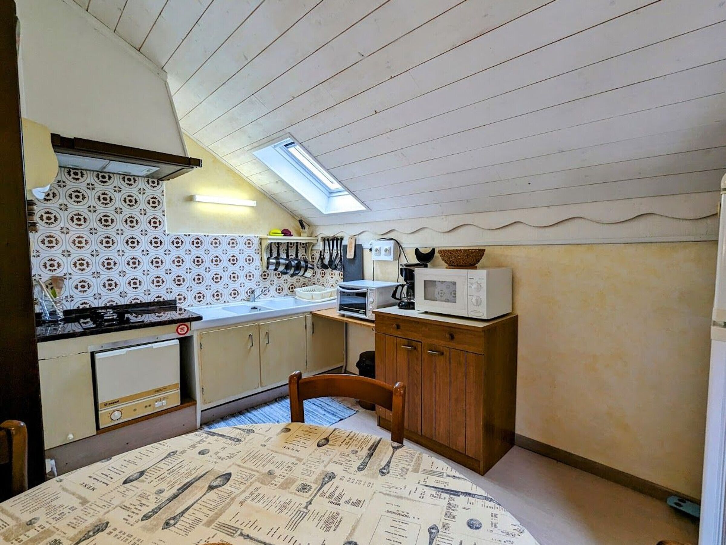 A compact kitchen with a sloped ceiling, a small dining table, and basic appliances.
