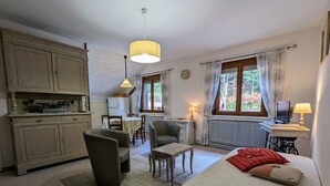 A cozy room with a bed, a desk, a chair, and a dining table. There is a window with curtains, a radiator, and a lamp on the desk. - Charming Renovated Farmhouse, Near Ski Resorts & Hiking Trails, All-Inclusive, Close to Amenities (Le Syndicat)