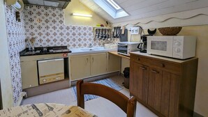 A compact kitchen with a gas stove, a microwave, a toaster, and a sink. There is a skylight above the sink, and the walls are decorated with patterned tiles. - Charming Renovated Farmhouse, Near Ski Resorts & Hiking Trails, All-Inclusive, Close to Amenities (Le Syndicat)