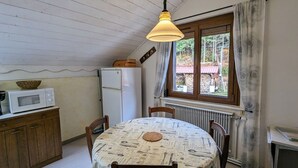 A compact kitchen with a dining table, a microwave, a refrigerator, and a hanging light fixture. - Charming Renovated Farmhouse, Near Ski Resorts & Hiking Trails, All-Inclusive, Close to Amenities (Le Syndicat)