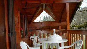 A wooden deck with a round table and two white plastic chairs.