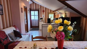 A cozy living room with a sofa, a dining table with a vase of flowers, and a kitchen in the background.