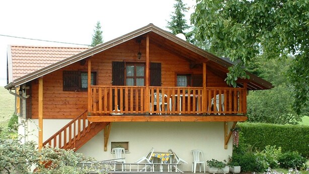 A wooden cabin with a balcony, a small porch area, and a garden with potted plants and flowers.
