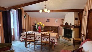A cozy dining area with a wooden table set for four, a fireplace, and a living room with a sofa and armchair.