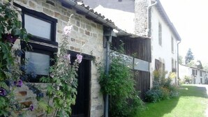 Une maison en pierre avec un petit jardin, une clôture en bois et un ciel dégagé.