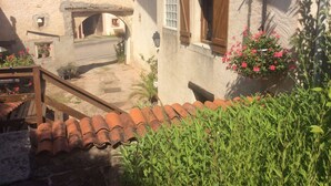A rustic courtyard with a stone wall, a wooden staircase, and a tiled roof.