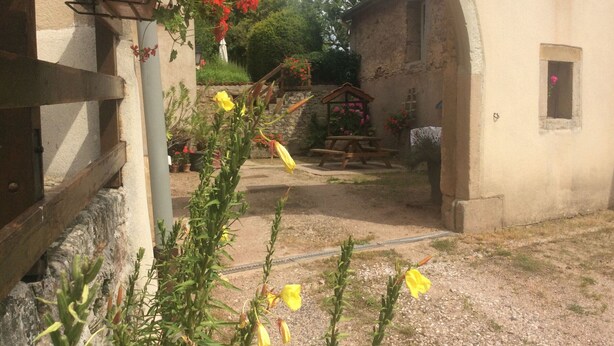 An outdoor courtyard with a rustic stone wall, a wooden bench, and a small wooden structure.