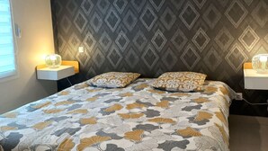 Een slaapkamer met een bed met een patroon, twee kussens, bedlampen en behang met een motief.
