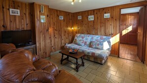 Une pièce aux murs lambrissés, comprenant un canapé, un divan en cuir, un téléviseur et une table sur laquelle se trouve un saladier.
