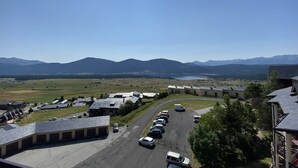 A parking lot with several cars, a building with a flat roof, and a mountainous landscape in the background. - T2 Apartment with balcony, equipped kitchen, parking (Les Angles)