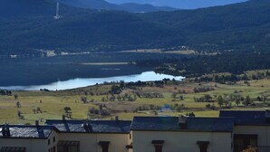A lakeside view with mountains in the background, a clear sky, and residential buildings in the foreground. - T2 Apartment with balcony, equipped kitchen, parking (Les Angles)
