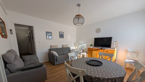 A modern living room with a grey sofa, a round table with a polka dot tablecloth, and a television on a wooden stand. - T2 Apartment with balcony, equipped kitchen, parking (Les Angles)