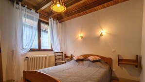 A bedroom with a wooden bed, white curtains, a radiator, and wall-mounted lights. - Charming Mountain Cottage with Ski Access, WiFi, and Family Amenities in La Bresse (La Bresse)