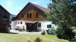 A two-story wooden house with a red-tiled roof, a patio with outdoor furniture, and a small garden area. - Charming Mountain Cottage with Ski Access, WiFi, and Family Amenities in La Bresse (La Bresse)