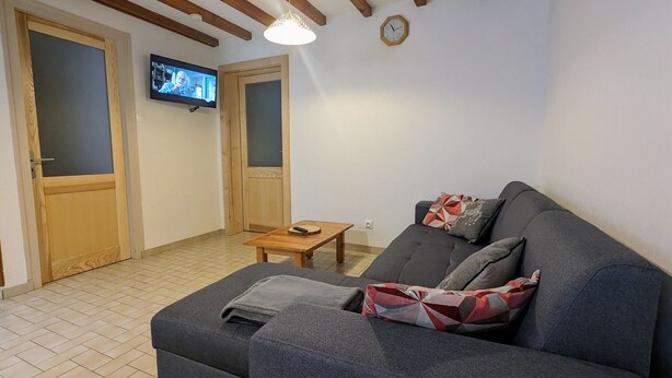 A living room with a grey sofa, a wooden coffee table, and a TV mounted on the wall. - Charming Mountain Cottage with Ski Access, WiFi, and Family Amenities in La Bresse (La Bresse)