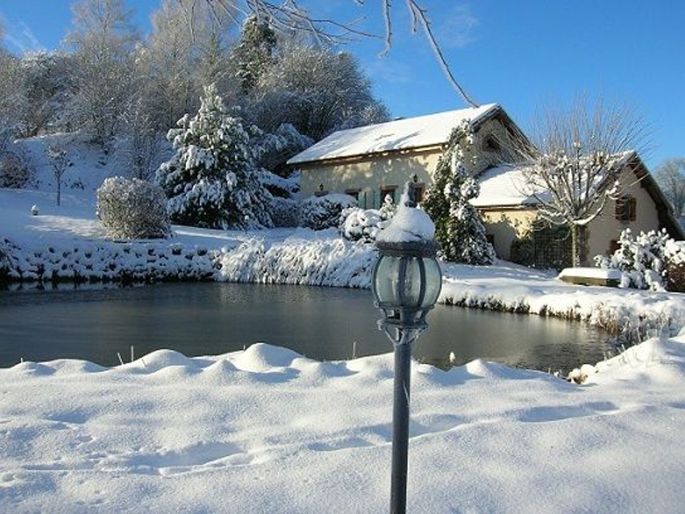 A snow-covered landscape with a house and a pond.
