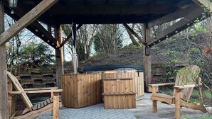 Un espace extérieur aménagé en bois, comprenant un jacuzzi, des chaises en bois et un patio couvert.