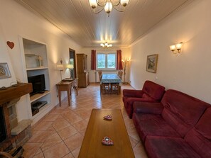 A living room with a fireplace, a red sofa, a wooden coffee table, a dining table with chairs, and a chandelier.