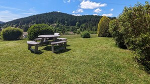 A picnic table in a grassy area with a mountain in the background. - Nature Getaway: Cozy Gîte, Near Ski Trails & Lake, Gérardmer (Gérardmer)