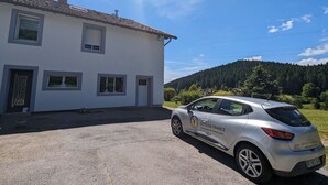 A white building with a tiled roof, a parked silver car with 'Gites de France' branding, and a forested hill in the background. - Nature Getaway: Cozy Gîte, Near Ski Trails & Lake, Gérardmer (Gérardmer)
