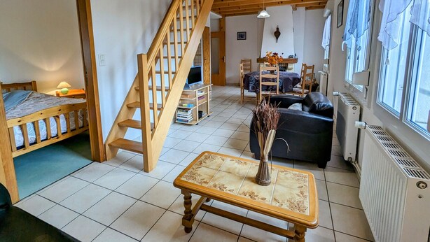 A spacious room with a wooden staircase, a bed, a dining table with chairs, a sofa, and a radiator. - Nature Getaway: Cozy Gîte, Near Ski Trails & Lake, Gérardmer (Gérardmer)