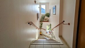 A staircase with a handrail, a window with a view of greenery, and a small shelf with a plant and picture frames. - Nature Getaway: Cozy Gîte, Near Ski Trails & Lake, Gérardmer (Gérardmer)