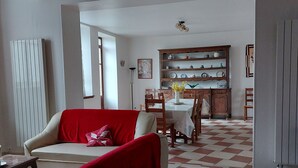 A living room with a red armchair, a dining area with a table and chairs, and a kitchen with shelves of dishes.