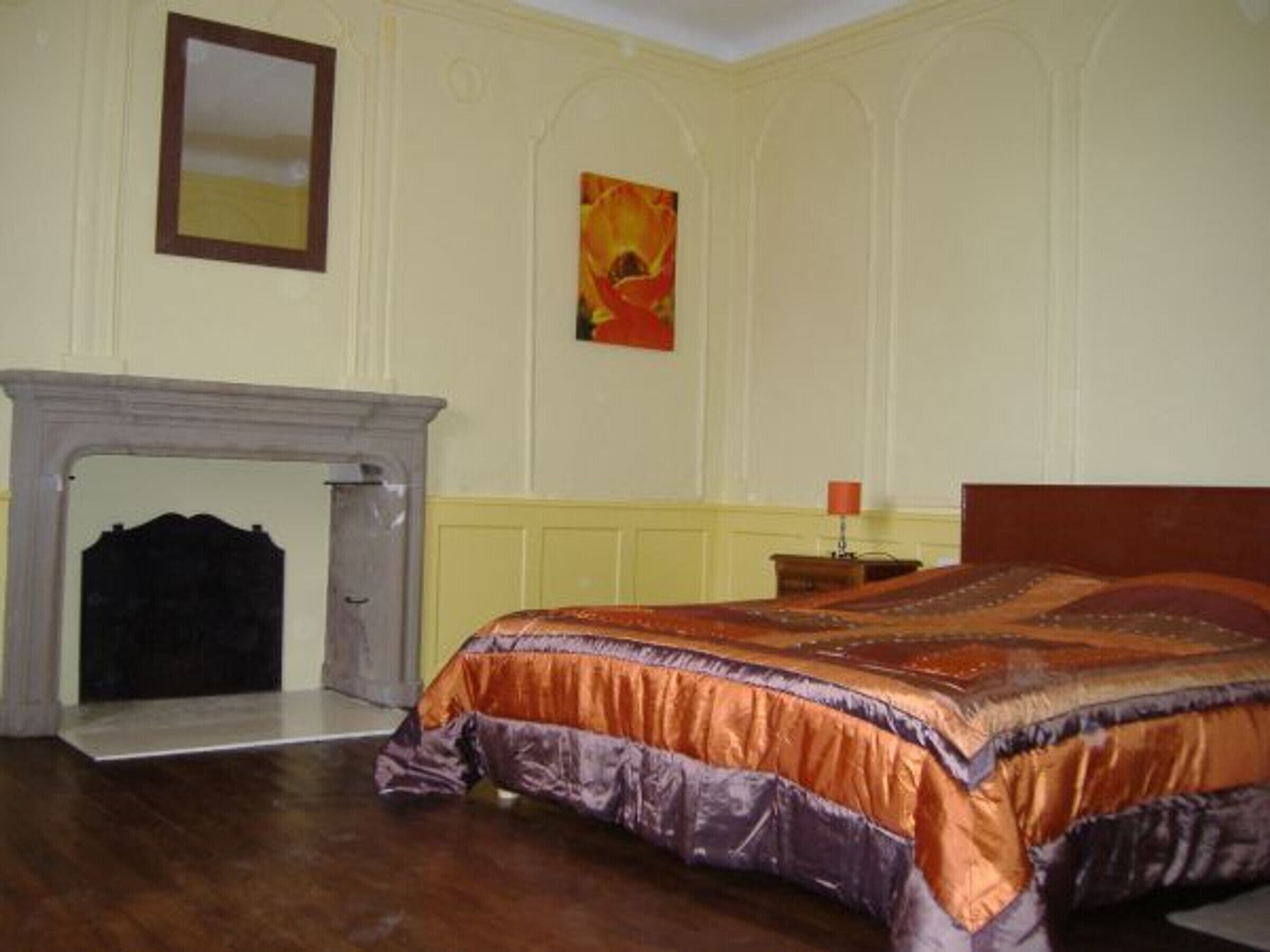 Une chambre à coucher avec un grand lit, une cheminée, une table de chevet et un tableau au mur.