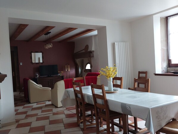 A dining area with a table set for four, wooden chairs, a vase with yellow flowers, and a television in the background.