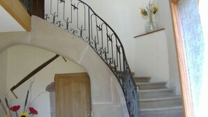 A curved staircase with a wrought iron railing, a wooden door at the bottom, and a vase with flowers on a shelf.