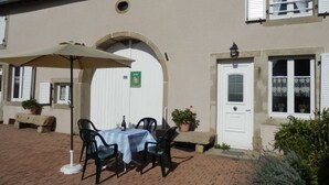 An outdoor patio with a table and chairs, a covered umbrella, and potted plants. - Charming Riverside Cottage with Modern Amenities & Scenic Views - 28 Rue du Charmont, Lironcourt (Lironcourt)